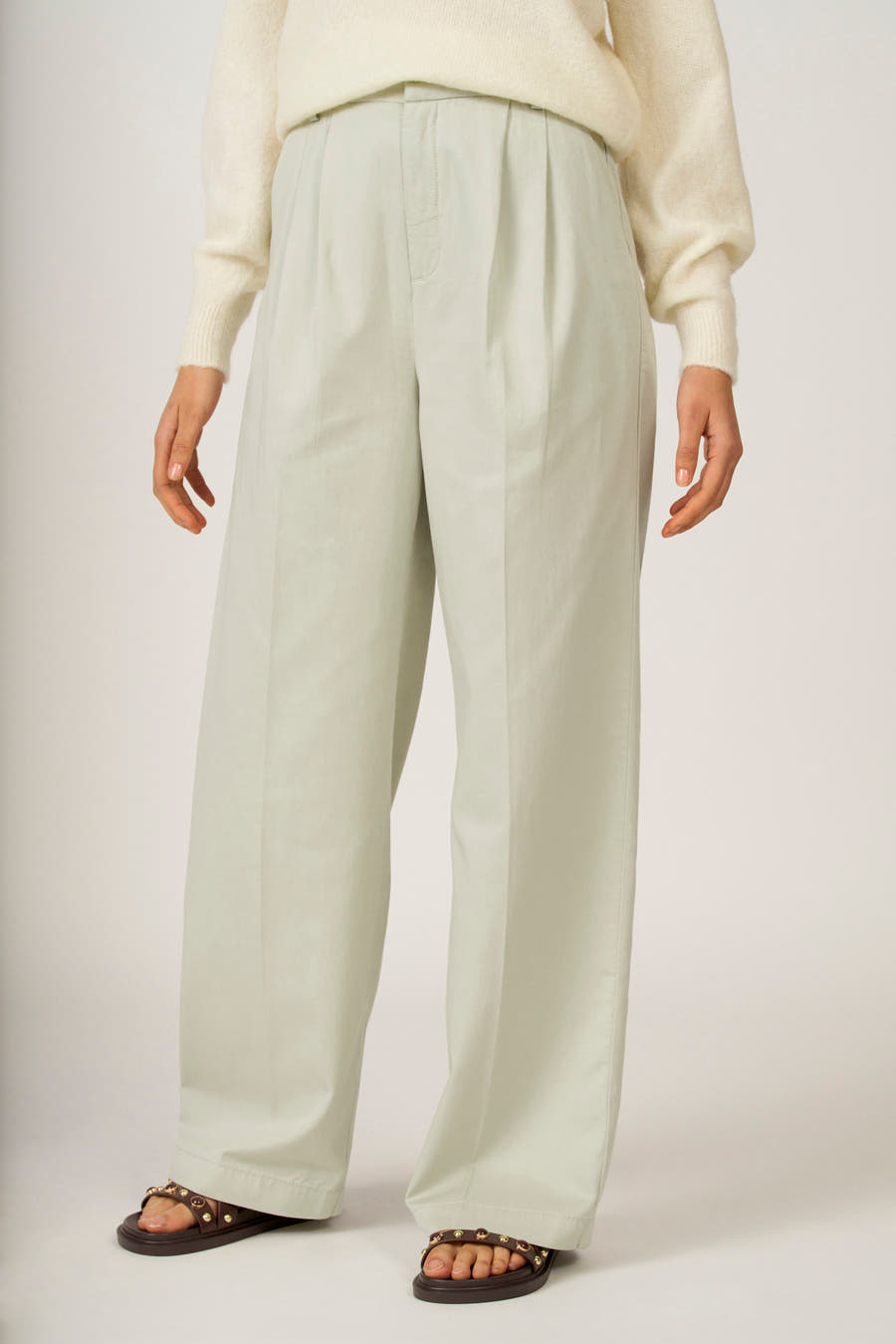 Groene colorbroek van Astrid Black Label, met plooien en wijde pijpen, gecombineerd met een gebreide trui en sandalen.