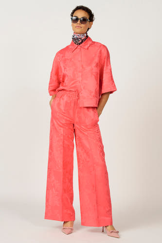 Roze blouse van Astrid Black Label, met bloemmotief en gedragen met een bijpassende broek en zonnebril.