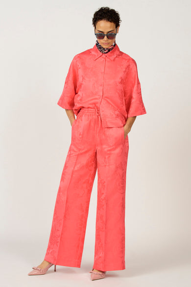 Pantalon rose d'Astrid Black Label, avec un motif floral et associé à une blouse rose et des chaussures.