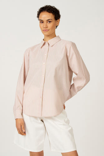 Chemise rose à manches longues d'Astrid Black Label, avec des rayures verticales et un pli au dos, portée avec un short blanc.