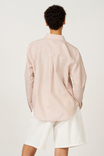 Roze hemd met lange mouwen van Astrid Black Label, met verticale strepen en een rugplooi, gedragen met witte shorts.
