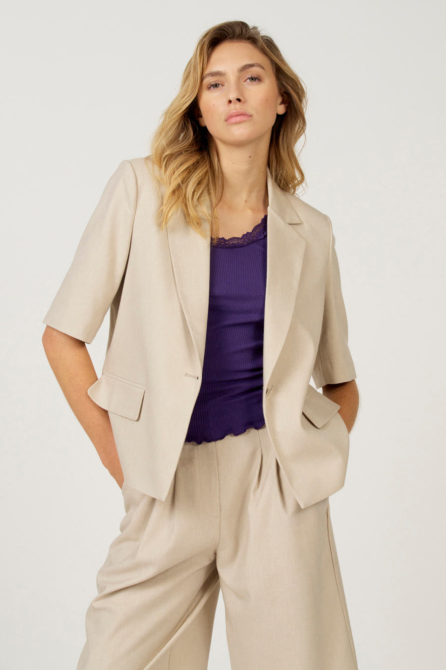 Ecru blazer van Astrid Black Label, gedragen met een paarse top met kanten rand en bijpassende broek.