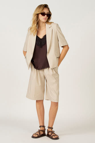Couleur écru bermuda d'Astrid Black Label, associée à une chemise brune et des sandales en cuir.