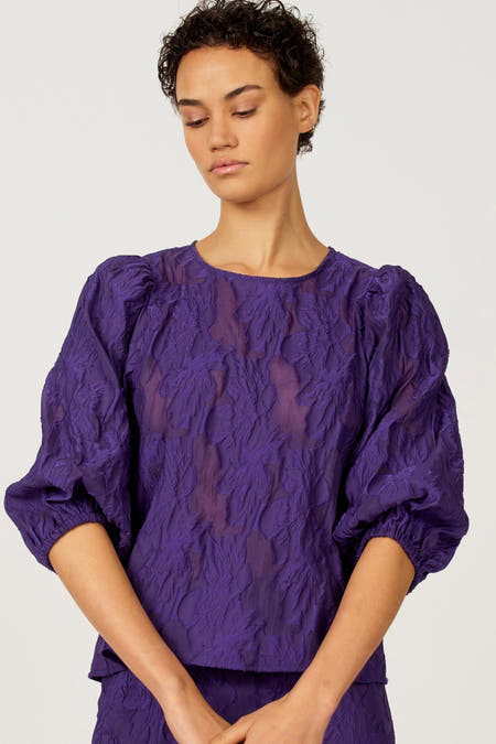 Paarse blouse van Astrid Black Label met een jacquard bloemmotief en pofmouwen.
