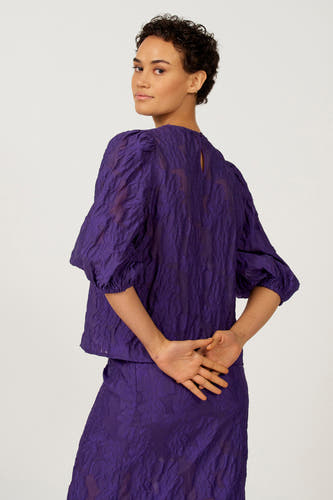 Paarse blouse met driekwart mouwen van Astrid Black Label, met een getextureerd bloempatroon en een sleutelgat detail aan de achterkant.