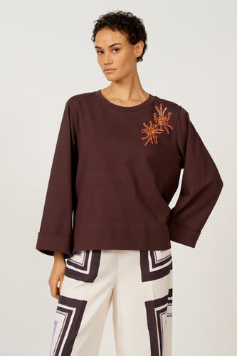 T-shirt marron à manches longues d'Astrid Black Label, avec des manches retroussées, associé à un pantalon à motif noir et blanc.