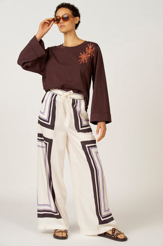 Bruin T-shirt met lange mouwen van Astrid Black Label, met oranje sierdetails en gedragen met een gestreepte broek.