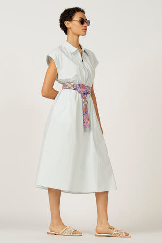 Tunique bleue sans manches d'Astrid Black Label, avec une ceinture colorée à la taille et des chaussures ouvertes.