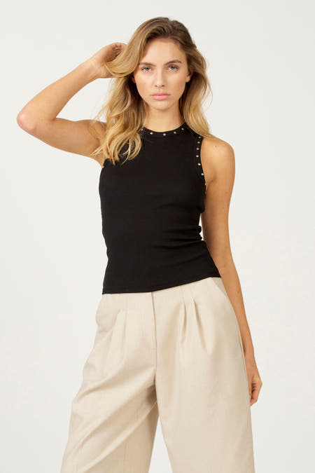 Zwarte singlet van Astrid Black Label met zilverkleurige studs langs de halslijn en armsgaten, gedragen met beige broek.
