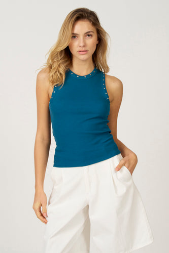 Blauwe singlet van Astrid Black Label met zilveren studs langs de halslijn en armsgaten, gedragen met een witte broek.
