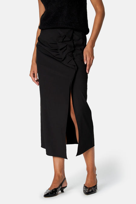 Jupe noire midi Astrid Black Label portée, avec volants à l’avant et fente sur le devant.