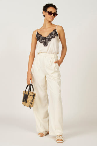 Witte broek van Astrid Black Label, met wijde pijpen, gecombineerd met een satijnen top met kanten details en sandalen.