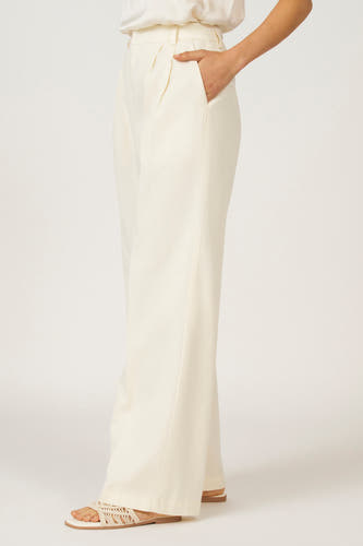 Witte broek van Astrid Black Label, met een hand in de zak en geweven sandalen.
