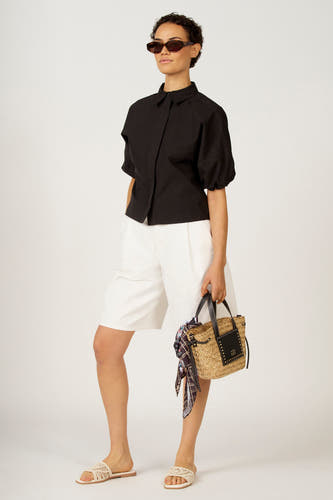 Zwarte blouse van Astrid Black Label, met korte mouwen en gedragen met witte shorts en een gevlochten tas.