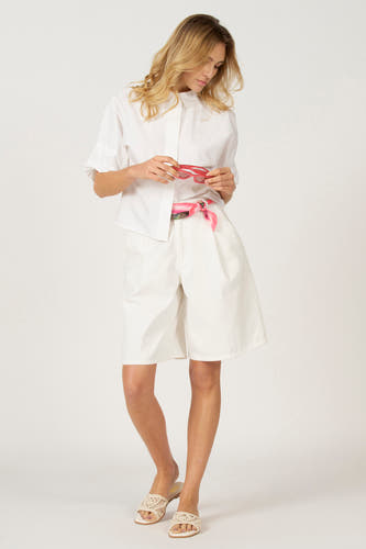 Blouse blanche à manches trois-quarts d'Astrid Black Label, portée avec des shorts bermuda blancs et des sandales.