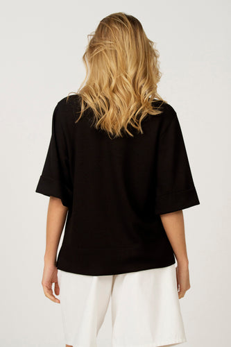 Zwart T-shirt met korte mouwen van Astrid Black Label, met omgeslagen mouwen en gedragen met een witte broek.
