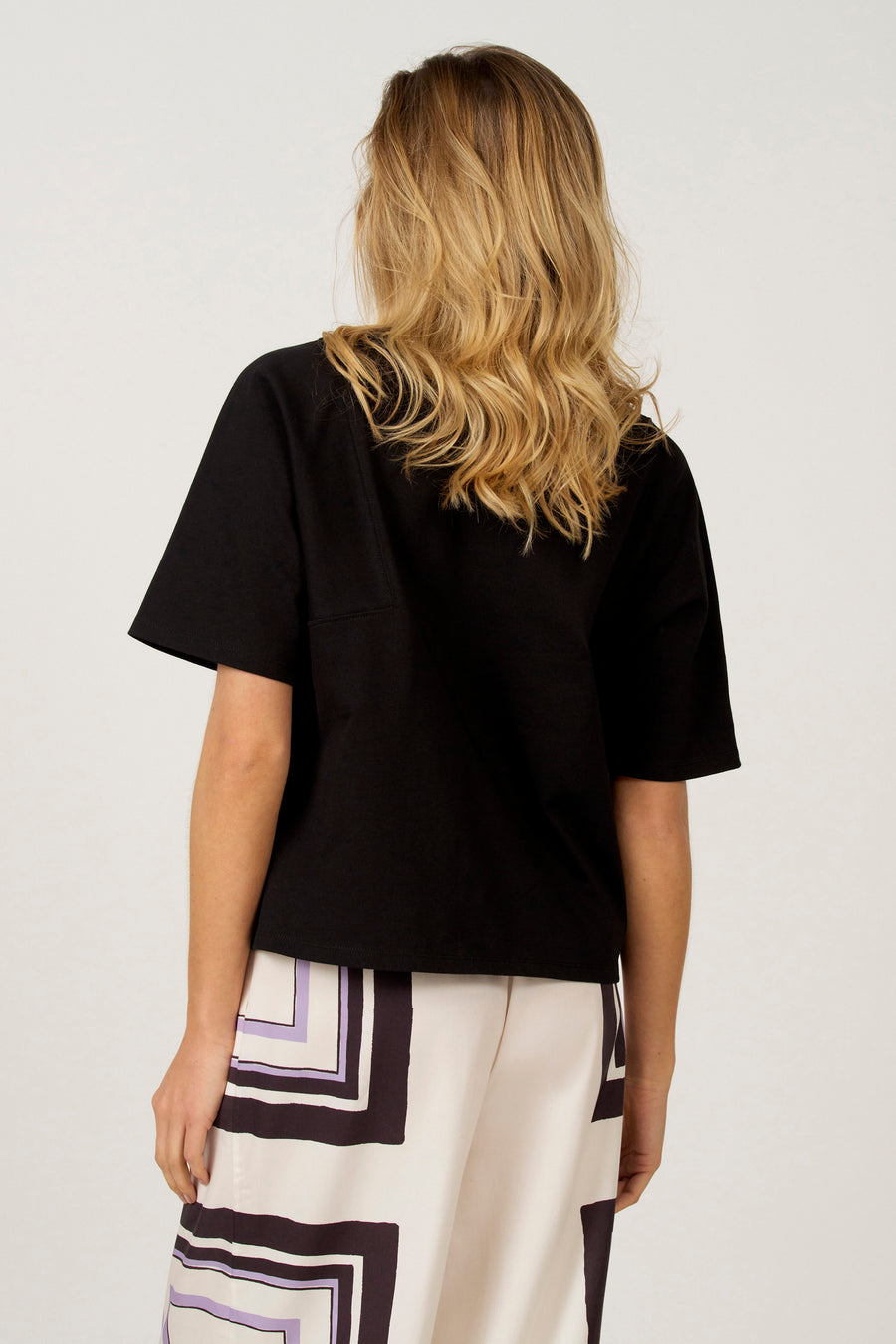 Zwart T-shirt met korte mouwen van Astrid Black Label, achterkant, gecombineerd met een broek met geometrisch patroon.