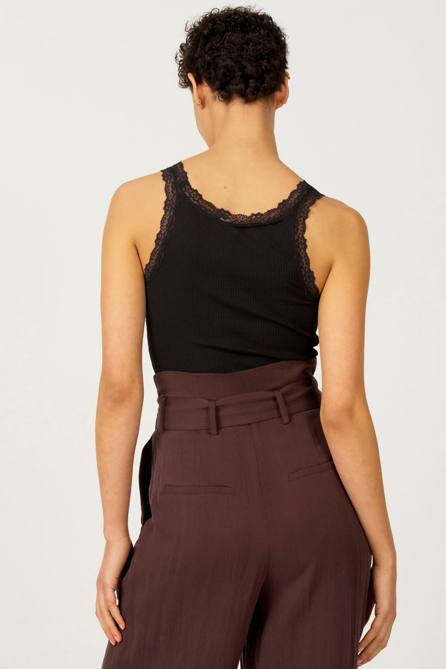 Zwarte singlet van Astrid Black Label met kanten details langs de halslijn en schouders, gedragen met een bruine pantalon.
