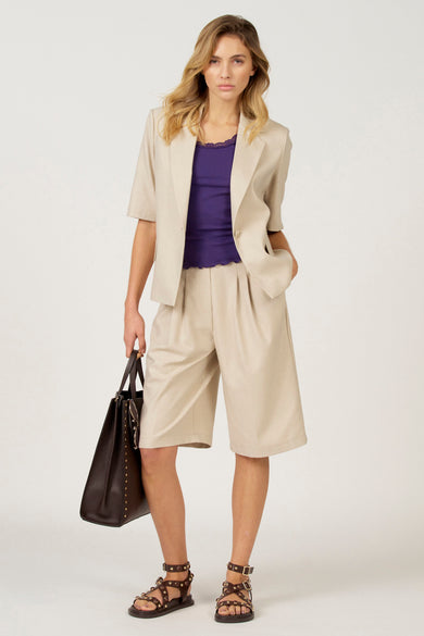 Paarse singlet van Astrid Black Label, gedragen onder een beige blazer en bijpassende bermuda, met bruine sandalen en een grote tas.
