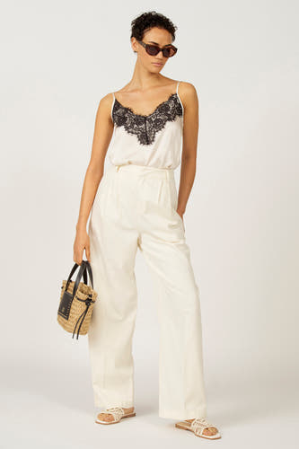 Ecru mouwloze blouse van Astrid Black Label, afgewerkt met zwart kant, gecombineerd met witte pantalon en een strokleurig tasje.
