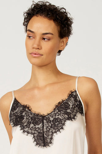 Vrouw met kort krullend haar, witte top met zwarte kanten details.