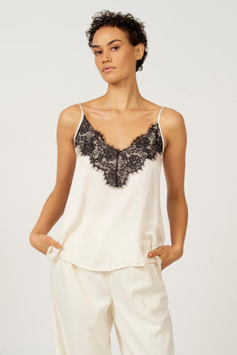 Ecru mouwloze blouse van Astrid Black Label met zwarte kanten details en bijpassende witte broek.