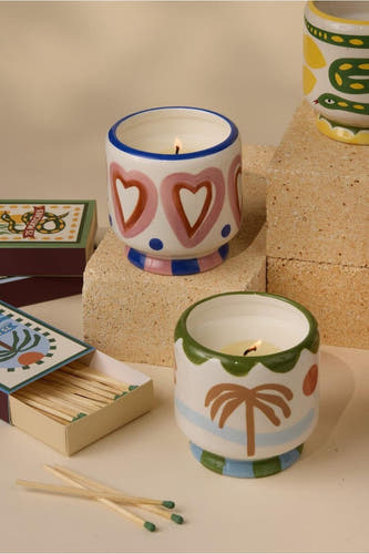 Meerkleurige kaarsen van PADDY WAX, met diverse patronen en decoratieve details, naast lucifersdozen.
