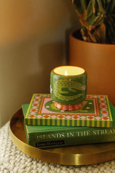 Groene kaars met krokodilprint van PADDY WAX, brandend op gestreept doosje, bovenop groen boek, op goudkleurig dienblad