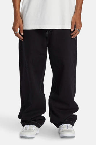 Zwarte wijde jeans van DC SHOES, met contrasterende stiksels en gecombineerd met een wit T-shirt en sneakers.
