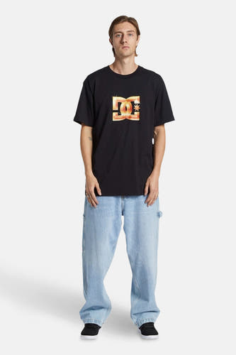 Wijde lichtblauwe denim jeans van DC Shoes, gedragen met een zwart T-shirt met logo en zwarte schoenen.