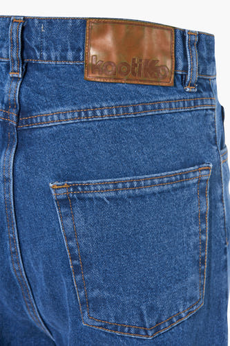Jean large bleu de KAOTIKO, avec un patch en cuir à l'arrière et des coutures orange.