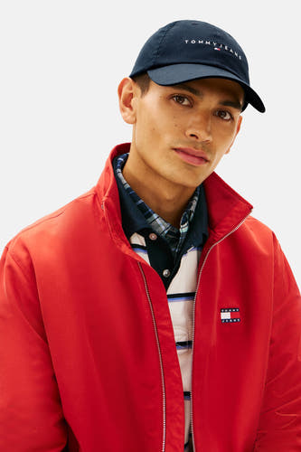 Chapeau bleu de Tommy Jeans avec le nom de marque brodé et veste bomber rouge.