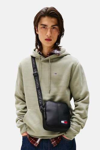 Sac à dos noir de Tommy Jeans avec une sangle ajustable et un logo, porté avec une hoodie olive et un chemisier rayé.