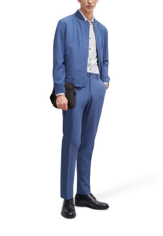 Zwarte schoudertas van TOMMY JEANS, gedragen door een man in blauw pak met een wit overhemd met print en zwarte schoenen.
