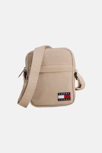 Sac à bandoulière beige de TOMMY JEANS, porté avec un pull vert olive, un pantalon noir et des mocassins.