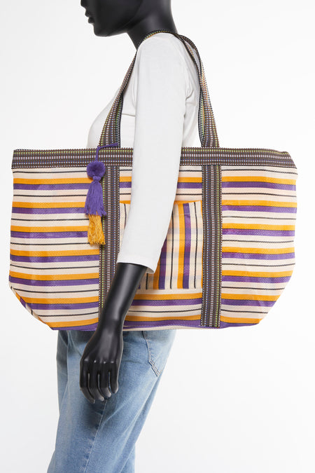 Sac à dos multicolore d'ALEX MAX, avec des rayures horizontales et un pinceau violet-or, porté avec une chemise blanche et un jean.