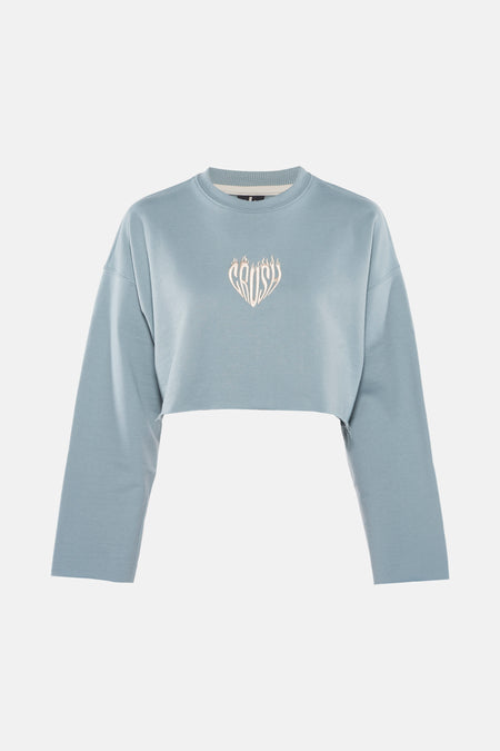Turquoise sweater van KAOTIKO, met een geborduurd logo in de vorm van een hart op de borst, cropped model.
