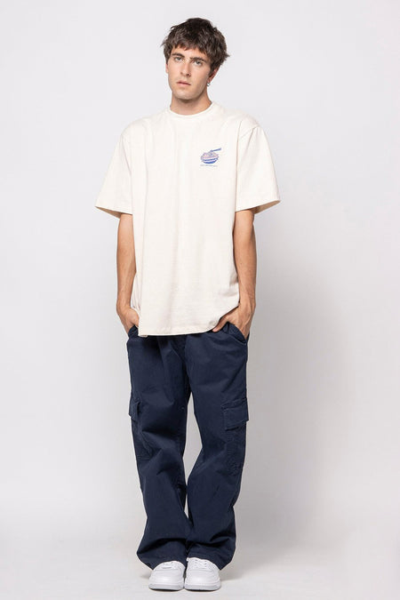 T-shirt écru à manches courtes de KAOTIKO avec petit logo bleu sur la poitrine, porté dans une photo lifestyle avec un pantalon cargo bleu marine et des baskets blanches