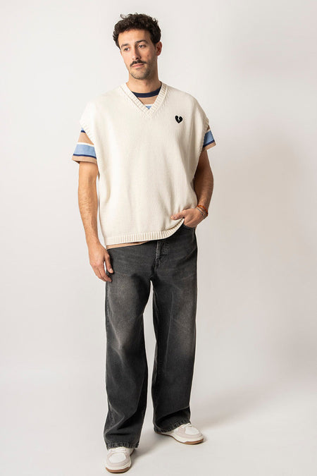 Ecru debardeur van KAOTIKO, met gebroken hart detail en gestreepte T-shirt eronder, gecombineerd met grijze jeans en witte sneakers.