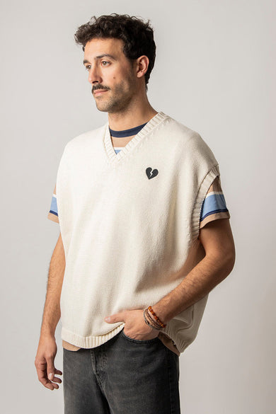 Ecru debardeur van KAOTIKO met gebroken hart detail, gedragen over een gestreept shirt en een zwarte jeans.
