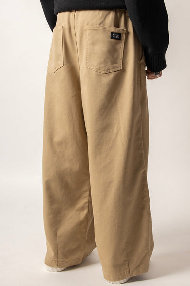Beige broek van KAOTIKO, met losse pasvorm, achterzakken en een zwarte merklabel.