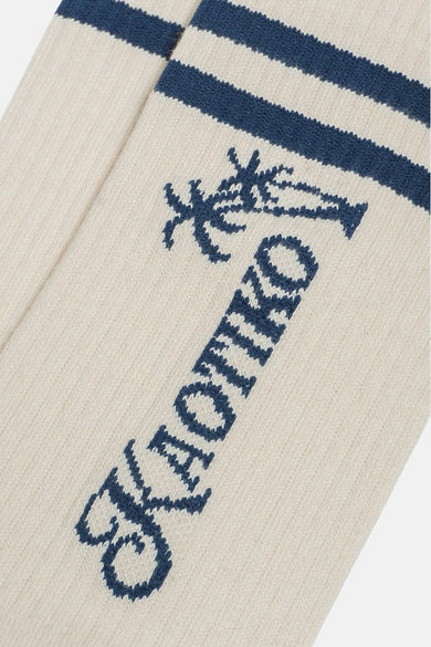 Ecru sokken van KAOTIKO met donkerblauwe strepen, een palmboom en de merknaam in blauw.

