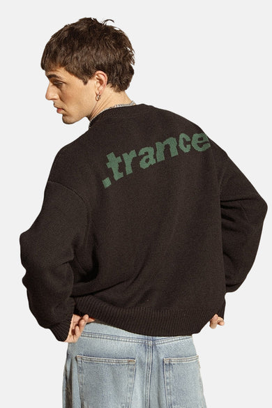 Pull noir avec col rond de KAOTIKO, avec une impression de texte verte sur le dos, porté avec des jeans bleus.