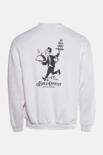 Witte sweater van KAOTIKO met een opdruk van een ober en de tekst "Bon Appétit" op de rug.
