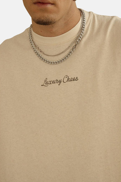 T-shirt écru à manches courtes de KAOTIKO, avec un slogan et porté avec des chaînes d'argent.
