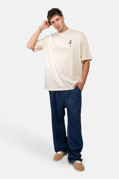 T-shirt écru à manches courtes de KAOTIKO, avec un petit imprimé, porté avec des jeans larges et des chaussures marron.