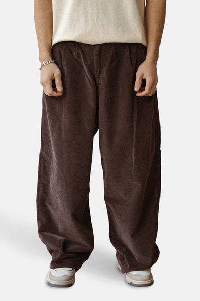 Bruine broek van KAOTIKO, met wijde pijpen en een lichte textuur, gecombineerd met een crèmekleurig shirt en zilveren armband.