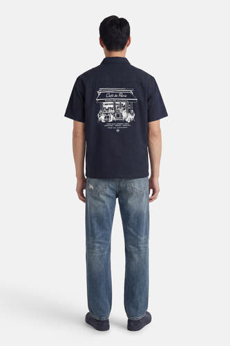 Blauw overhemd met korte mouwen van KAOTIKO, met witte Café de Paris print op de rug, gecombineerd met jeans.
