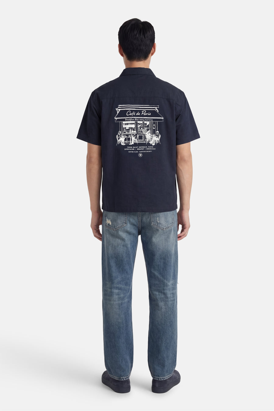 Blauw overhemd met korte mouwen van KAOTIKO, met witte Café de Paris print op de rug, gecombineerd met jeans.
