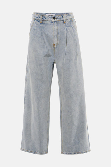Jean en denim bleu clair large de KAOTIKO, avec des plis et associé à un polo en maille marron et des baskets en daim.